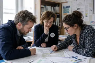 Local officials and a city worker in a Nantes municipal office, collaborating over documents and maps in a natural, focused setting