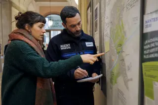 Municipal agent and activist intently discussing environmental plans in Nantes city hall corridor, natural light, candid moment.