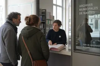 Citizens quietly consulting an official over public records in a glass-walled municipal archive, with a subtle reflection of a third person, all shown in a calm, administrative setting.